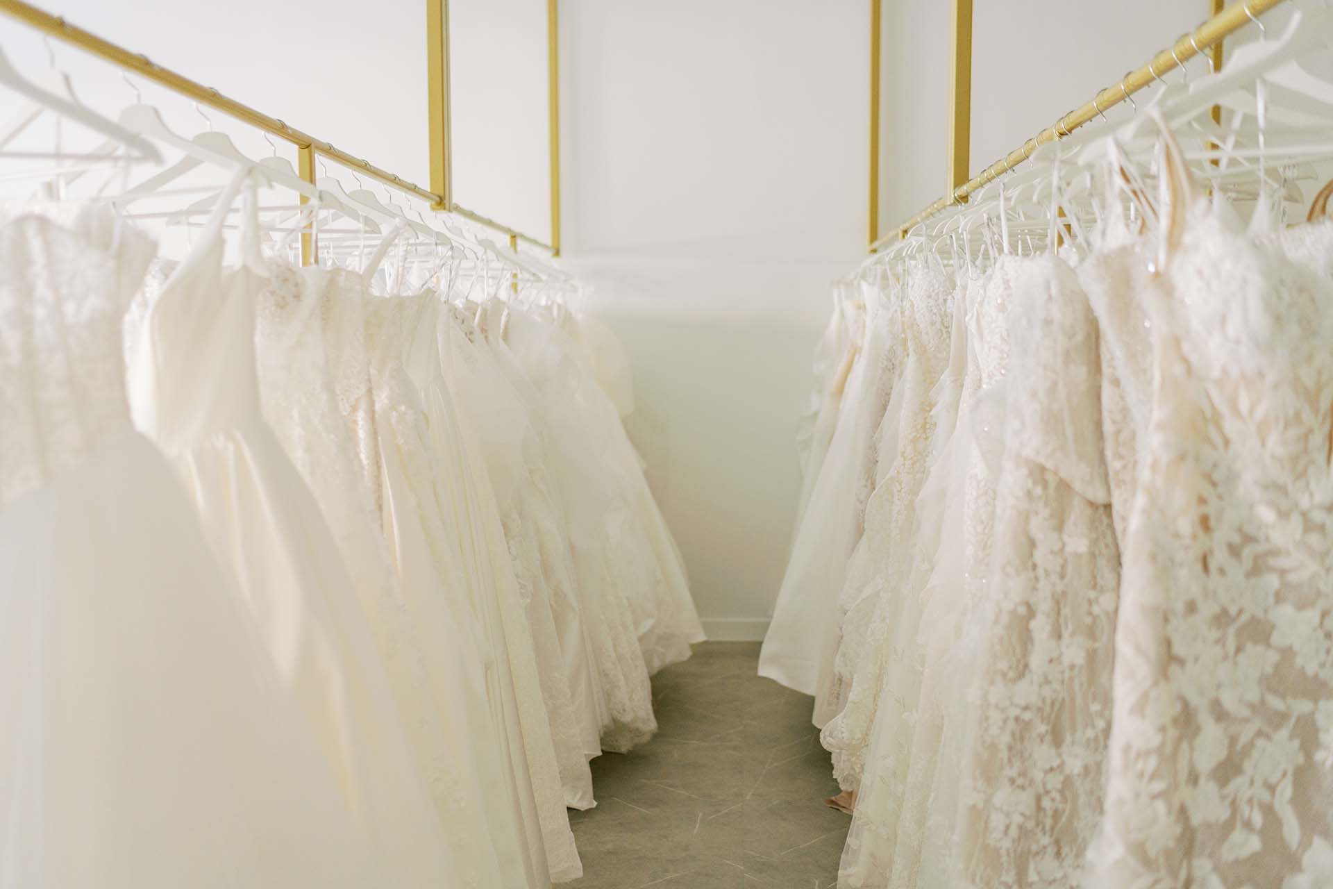 White and ivory wedding gowns displayed on gold clothing racks inside Hailey Nicole Bridal