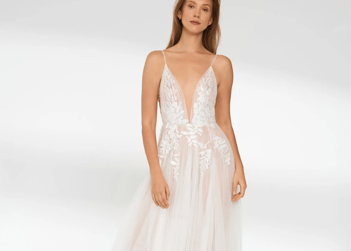 Romantic A-line wedding dress featuring a sheer bodice, deep V neckline, thin straps, and delicate floral lace appliqué over a soft tulle skirt