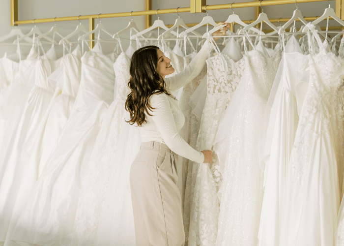 Bride browsing wedding dresses on a bridal boutique showroom rack.