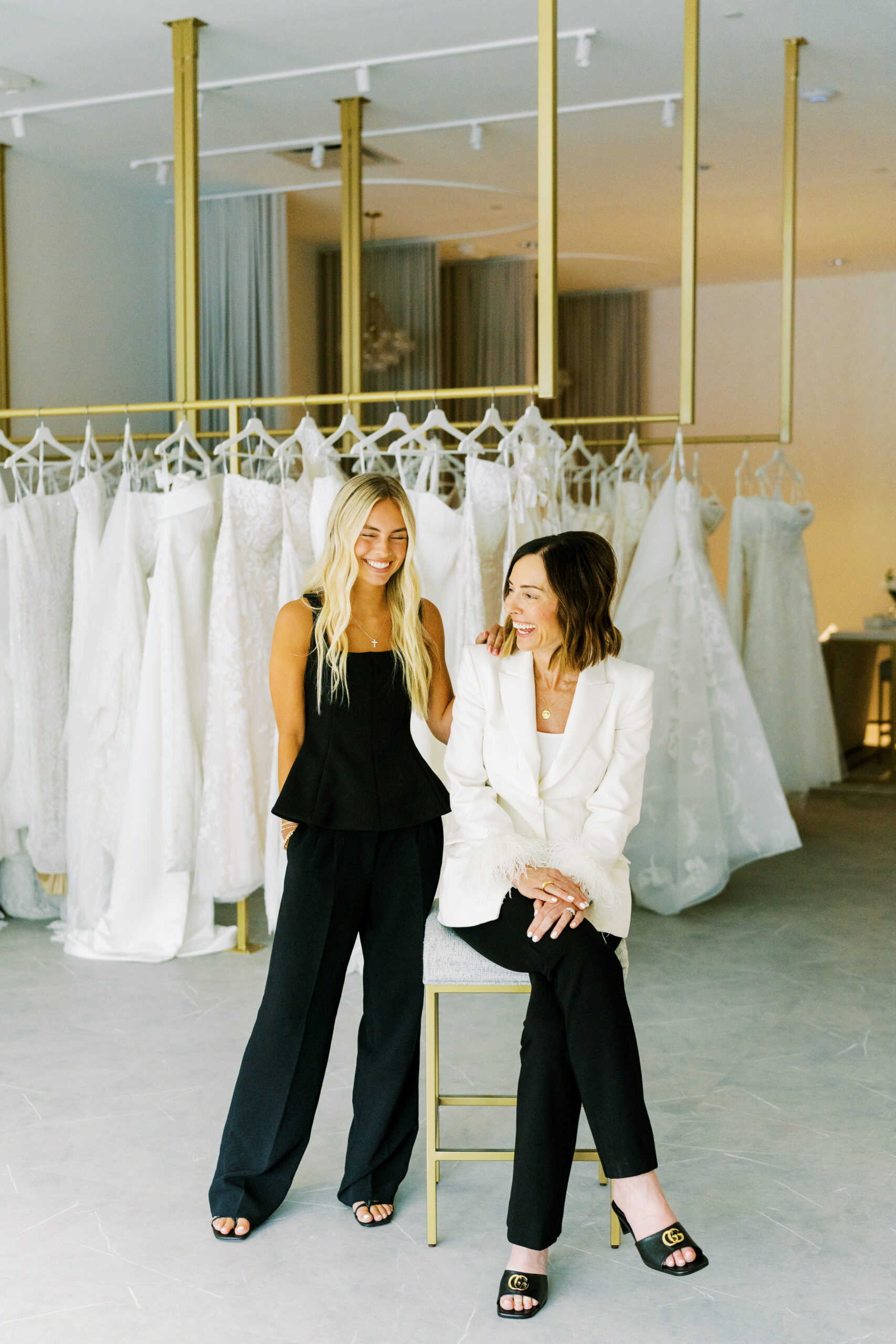 Two bridal boutique team members seated in front of a collection of wedding dresses