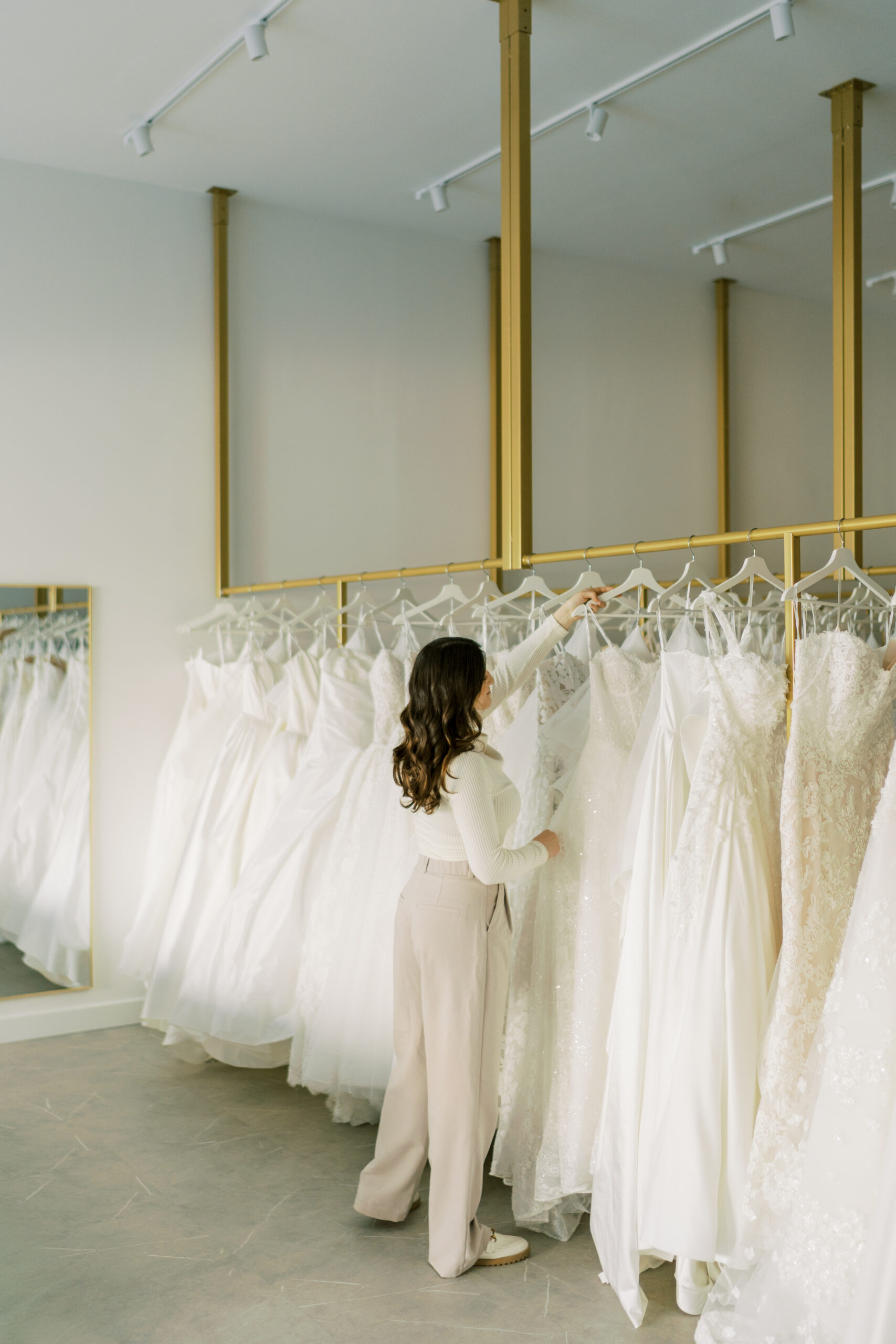 Hailey Nicole Bridal Bride looking through wedding gowns hanging on racks at Hailey Nicole Bridal
